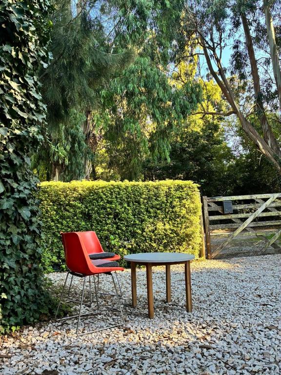 a red chair and a table in front of a hedge at Duplex Las Margaritas Bosque Peralta Ramos in Mar del Plata