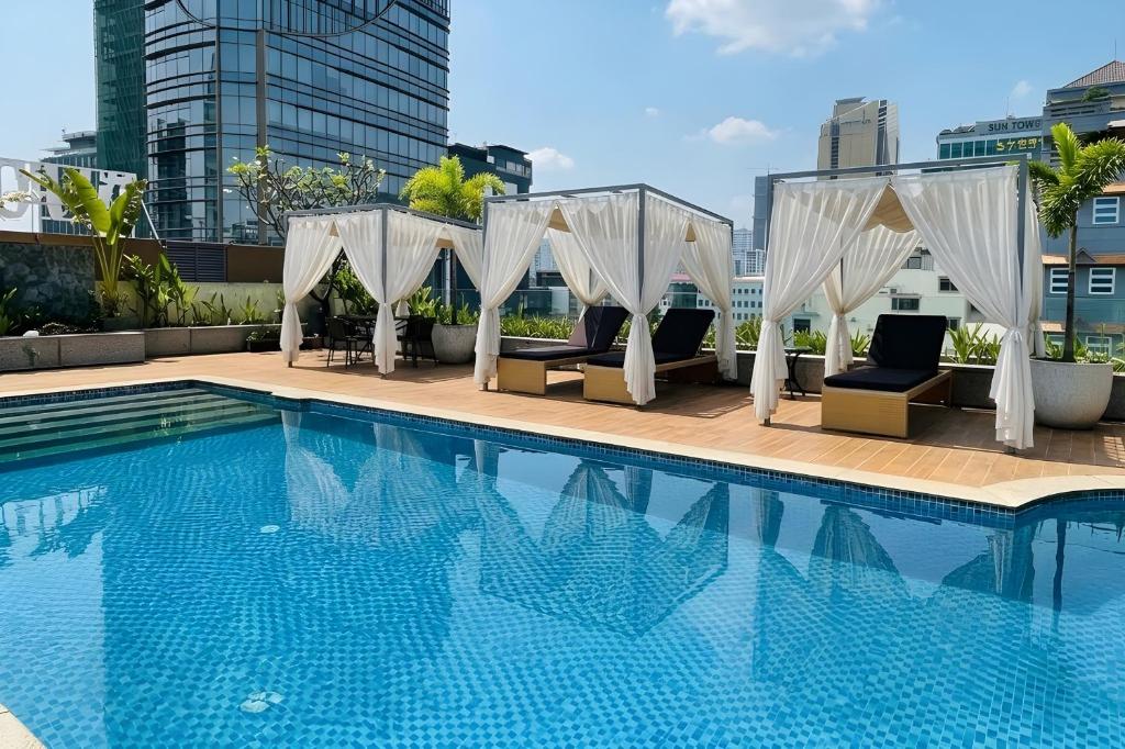 a swimming pool with white curtains and chairs next to a building at Clover Hotel Monivong in Phnom Penh