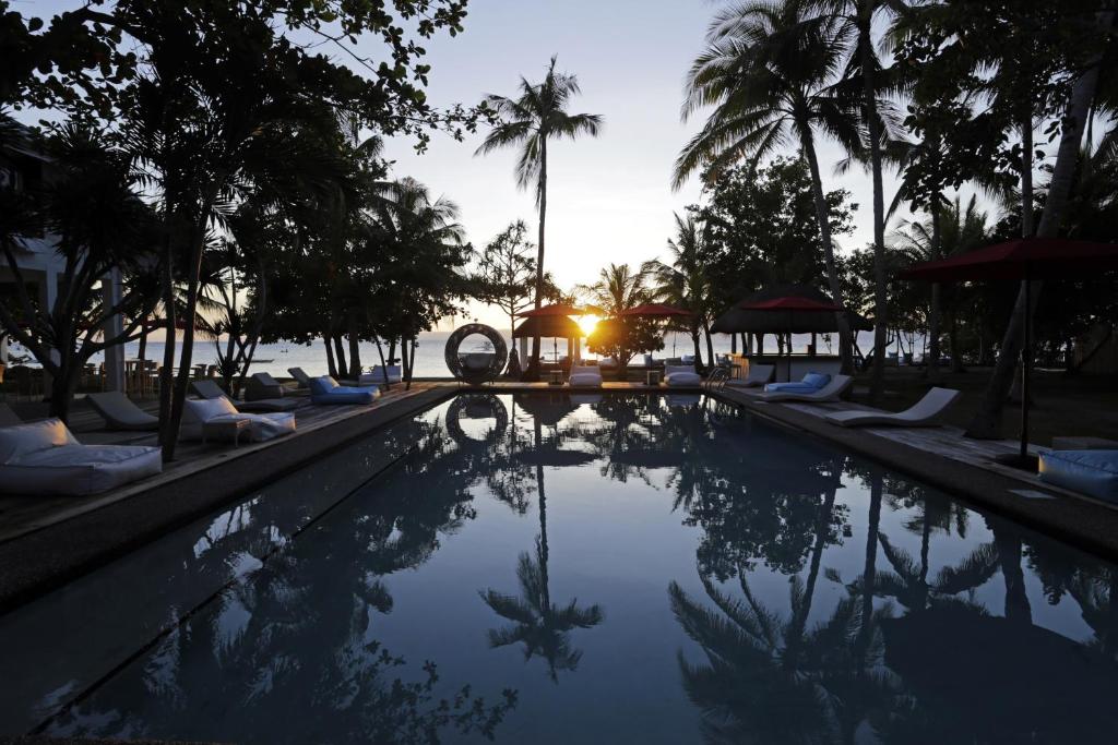 einen Pool in einem Resort mit Palmen und Sonnenuntergang in der Unterkunft Cabilao Sanctuary Beach & Dive Resort in Loon