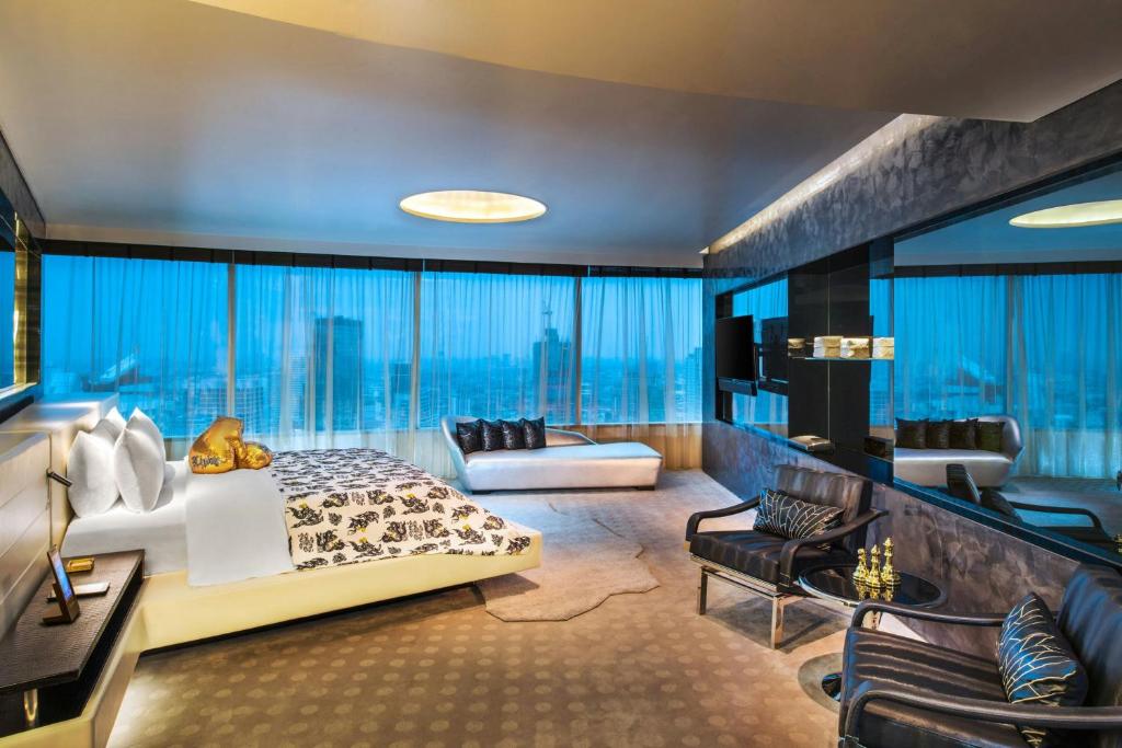 A dark, richly styled bedroom-lounge with a patterned bedspread and wraparound city windows.