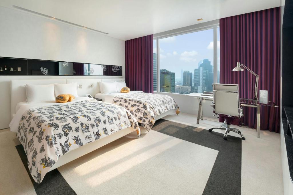 A bright twin room with two beds, a city-facing window and a compact work area.
