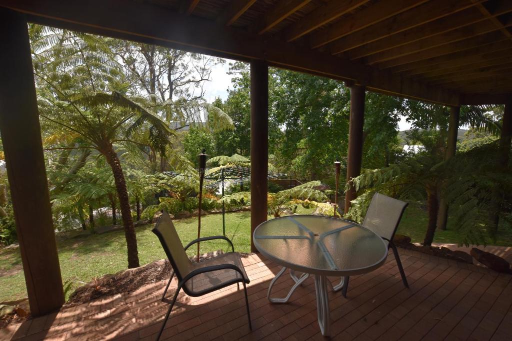 - une table en verre et 2 chaises sur une terrasse couverte dans l'établissement Rockwall Avoca Beach, à Avoca Beach