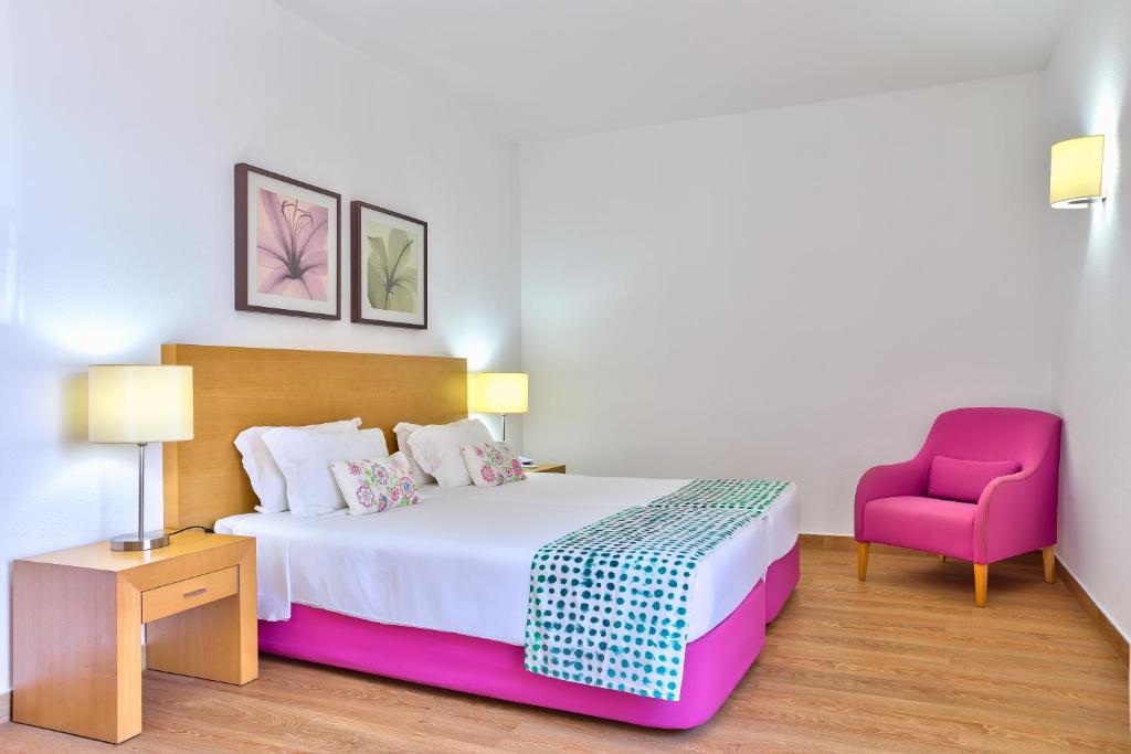 a bedroom with a bed and a pink chair at Hotel Torre Praia in Porto Santo