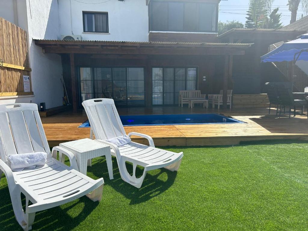two white chairs sitting on the grass near a pool at מבית תכלת בית של חופש Allentown 21 אלנטאון 21 in Tiberias