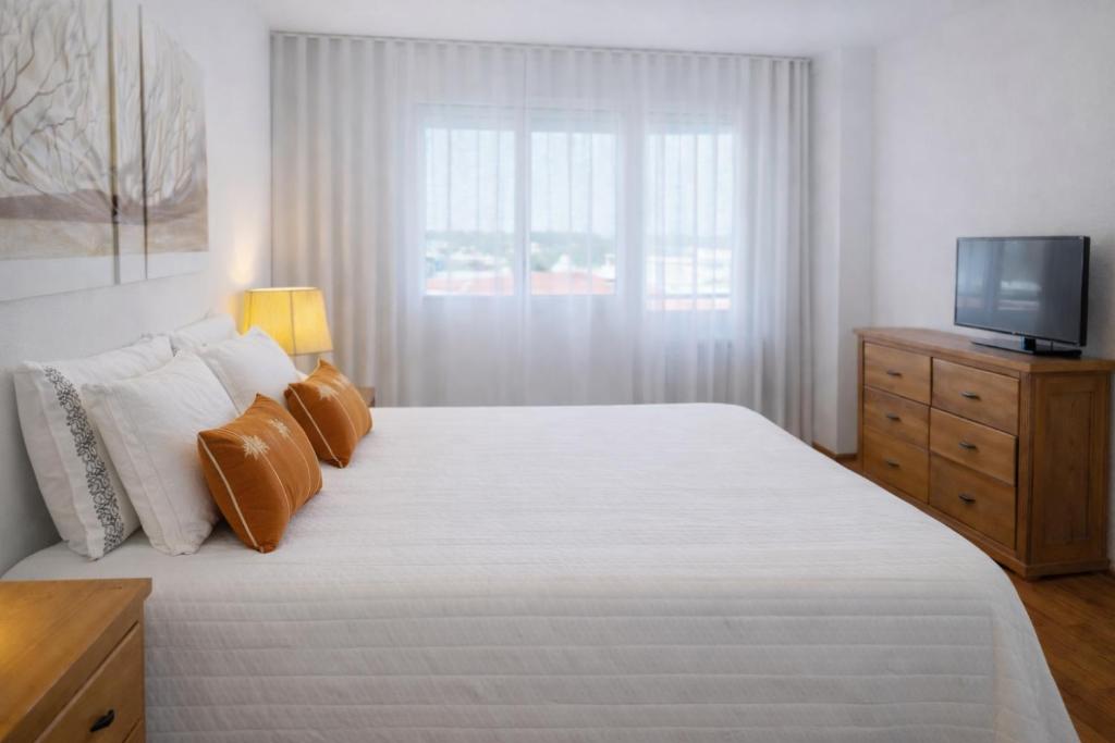 a bedroom with a large white bed with a television at Free Wave Rooms in Maia