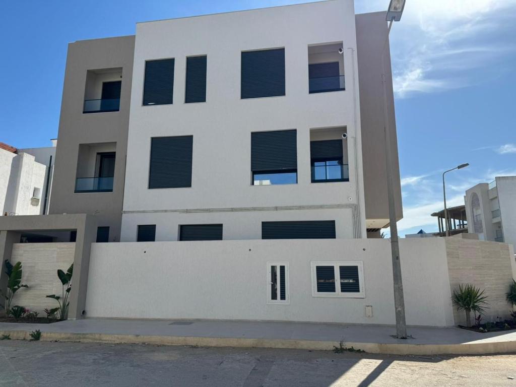 a white building with a fence in front of it at Résidence Jasmin in Harqalah