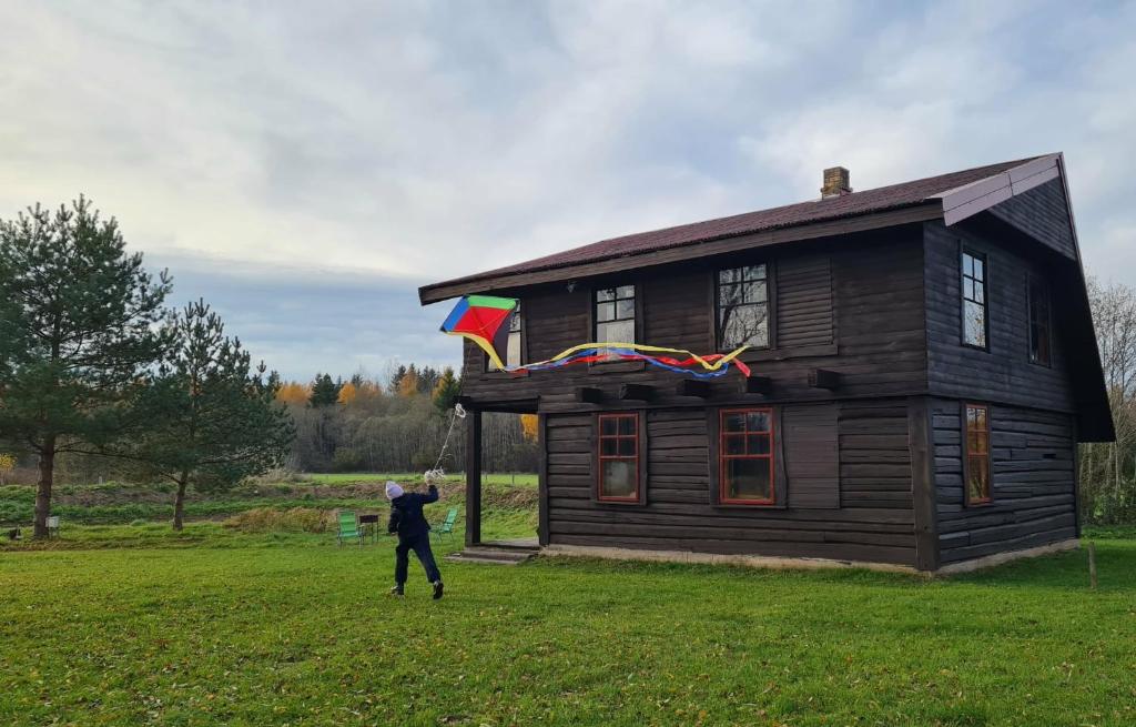 a man flying a kite in front of a log house at Viešnagė gamtos prieglobstyje in Gūragiai
