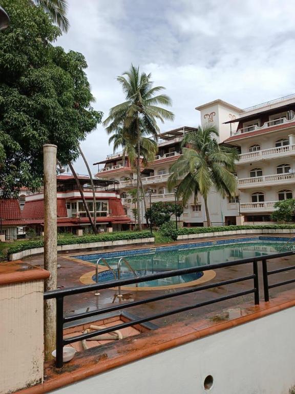 a swimming pool in front of a building with palm trees at Apartmentbyzaara in Colva