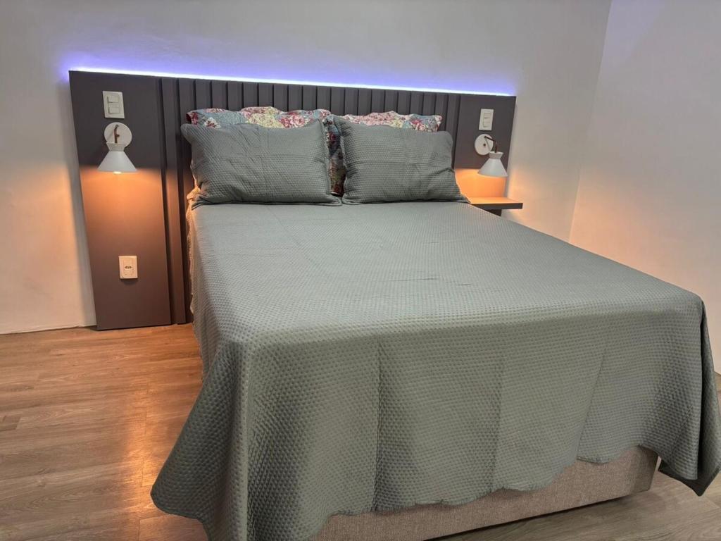 a bedroom with a bed with a green blanket and pillows at Estúdio com suíte super confortável no centro in Ijuí
