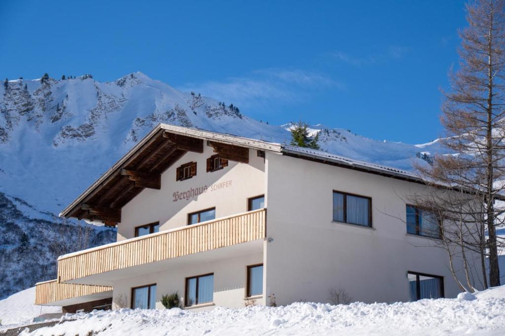 a building in the snow with mountains in the background at Berghaus Schäfer in Faschina