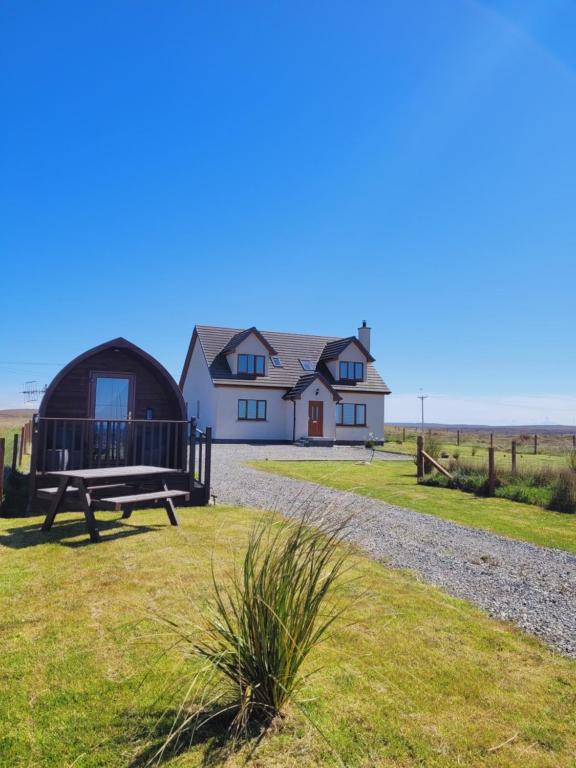 a large white house with a bench in front of it at Ocean View Glamping Pod in Borve