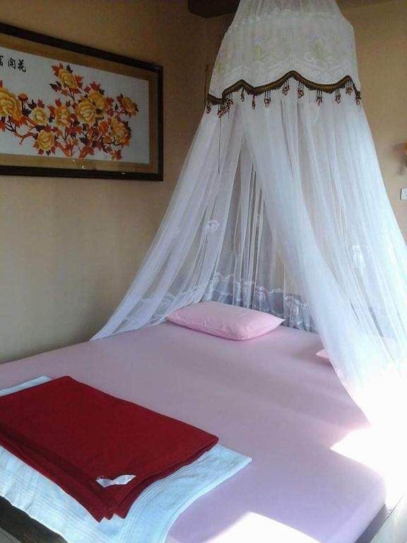 a white bed with a canopy and a red blanket at Monkey Business Tours & Accommodation in Bukit Lawang