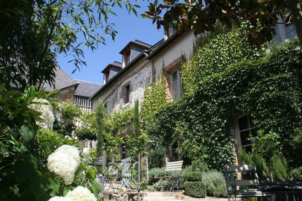 un edificio cubierto de hiedra con bancos y sillas en un jardín en La Cour Sainte Catherine demeure de charme en Honfleur