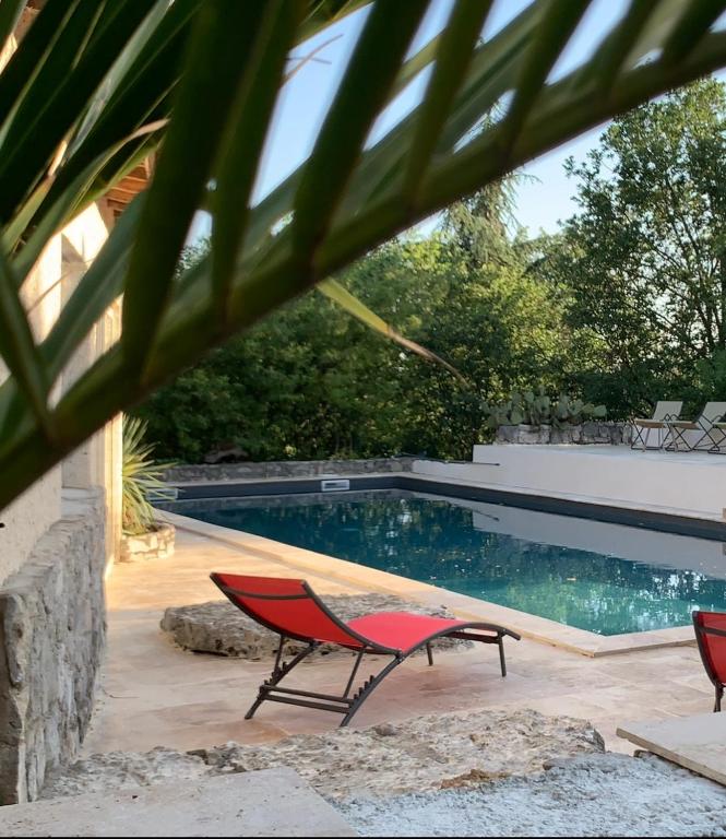 a swimming pool with two red chairs and a table at Le Mazet, studio climatisé avec accès piscine in Saint Alban Auriolles