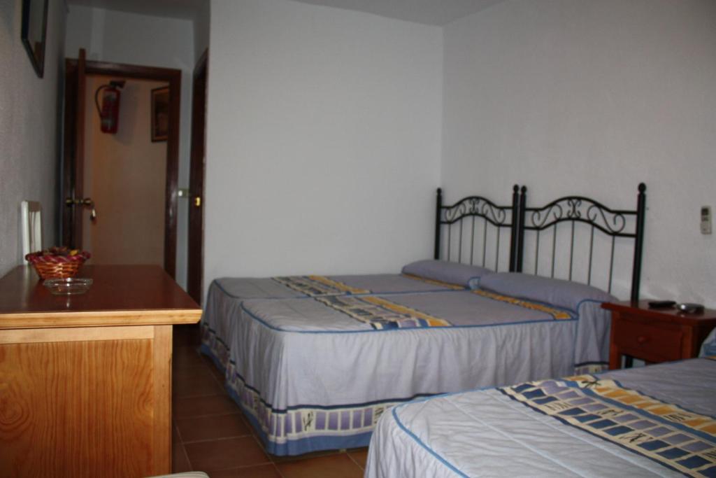1 dormitorio con 2 camas, mesa de madera y escritorio en Hostal Tamarindos, en Matalascañas