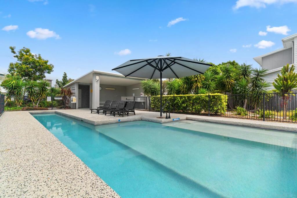 a swimming pool with an umbrella next to a house at Direct Collective - Breeze on Brightwater in Mooloolaba