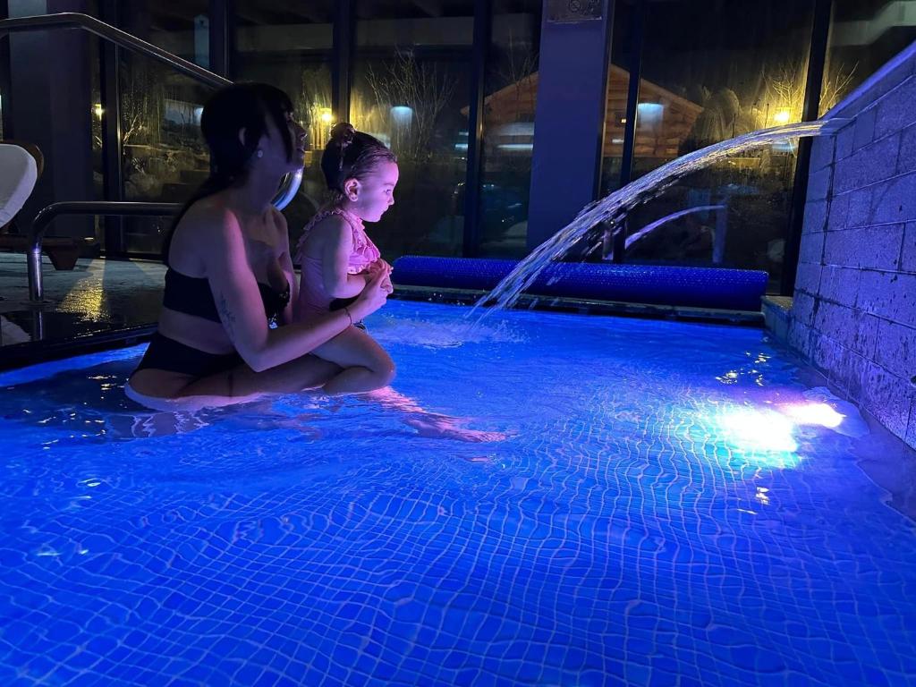 two girls sitting in a swimming pool at night at Q Resort and Spa in Săcele