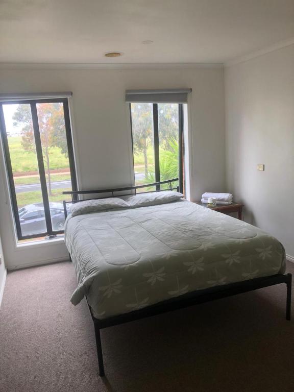 a bedroom with a bed and two large windows at Manors Bvld in Wyndham Vale