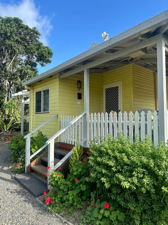 a yellow house with a white fence and flowers at Lemon Cottage in Rous Mill