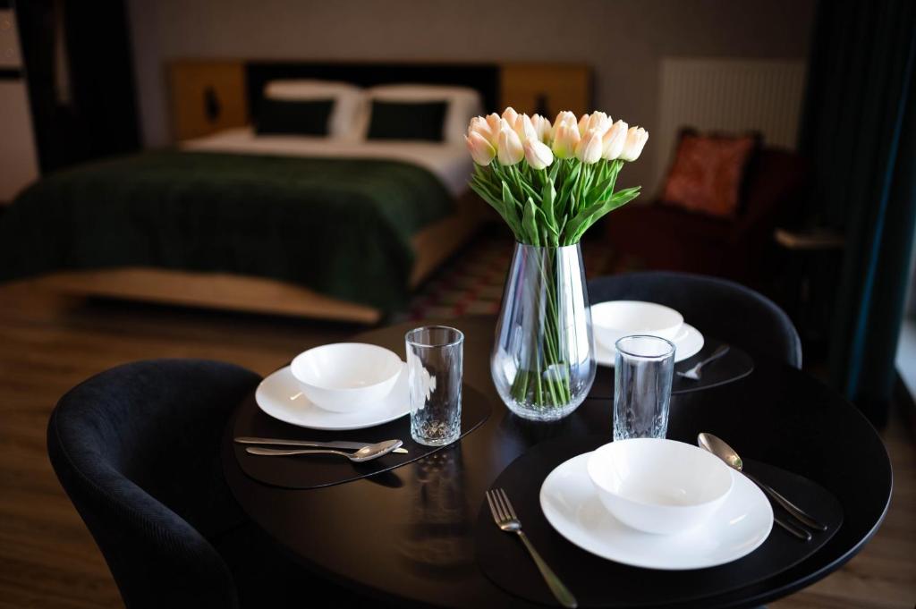 a table with white plates and a vase of flowers at Apartament Centrum z tarasem prywatny parking in Płock