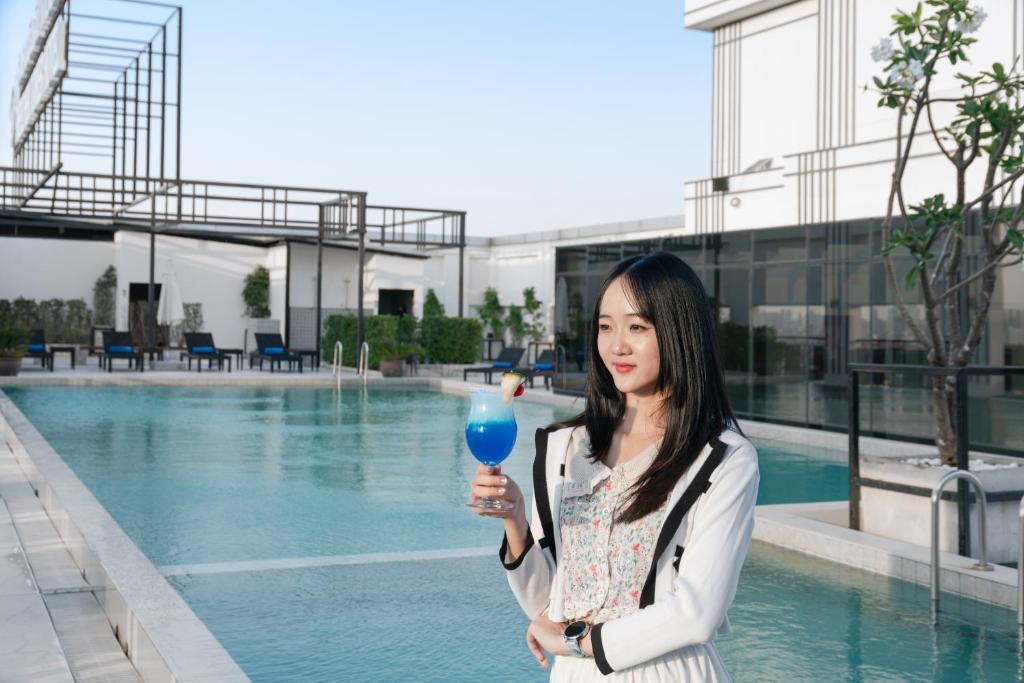 a woman holding a blue drink in front of a pool at SZ Canalside Hotel in Bangkok