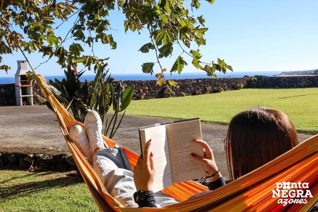 a woman laying in a hammock reading a book at Casa das Vaquinhas by Ponta Negra Azores in Altares