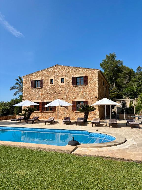 a building with a pool and chairs and umbrellas at Finca Es Puig, rustic estate with views in Es Carritxo