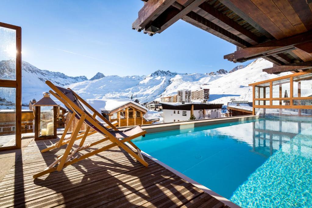 a pool with a chair on a deck with snow covered mountains at Hôtel les Campanules by Les Etincelles in Tignes