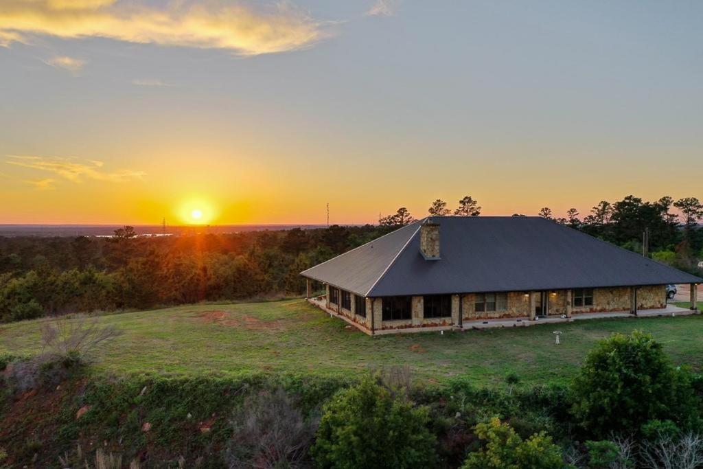 a house on a field with the sunset in the background at Hilltop Bastrop Retreat in Bastrop
