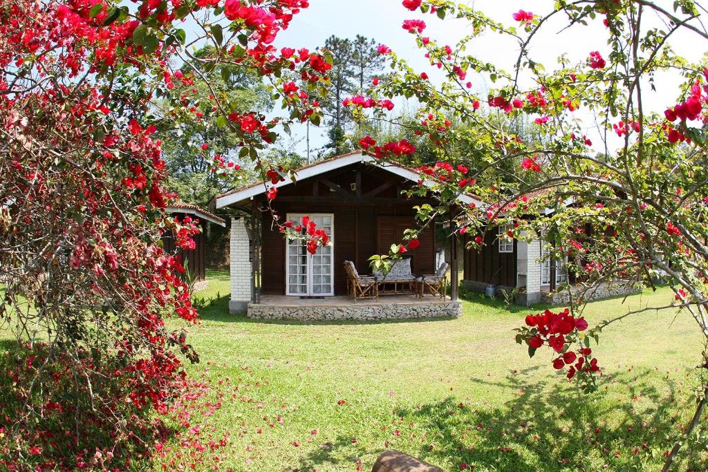 a cabin with a table and chairs in a yard with red flowers at Chalé Ipê Amarelo in Juquitiba