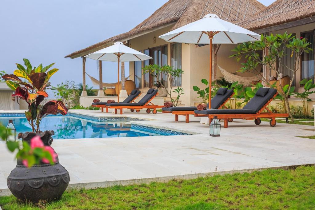 a resort pool with lounge chairs and an umbrella at Sunhouse, Mandala Village in Uluwatu