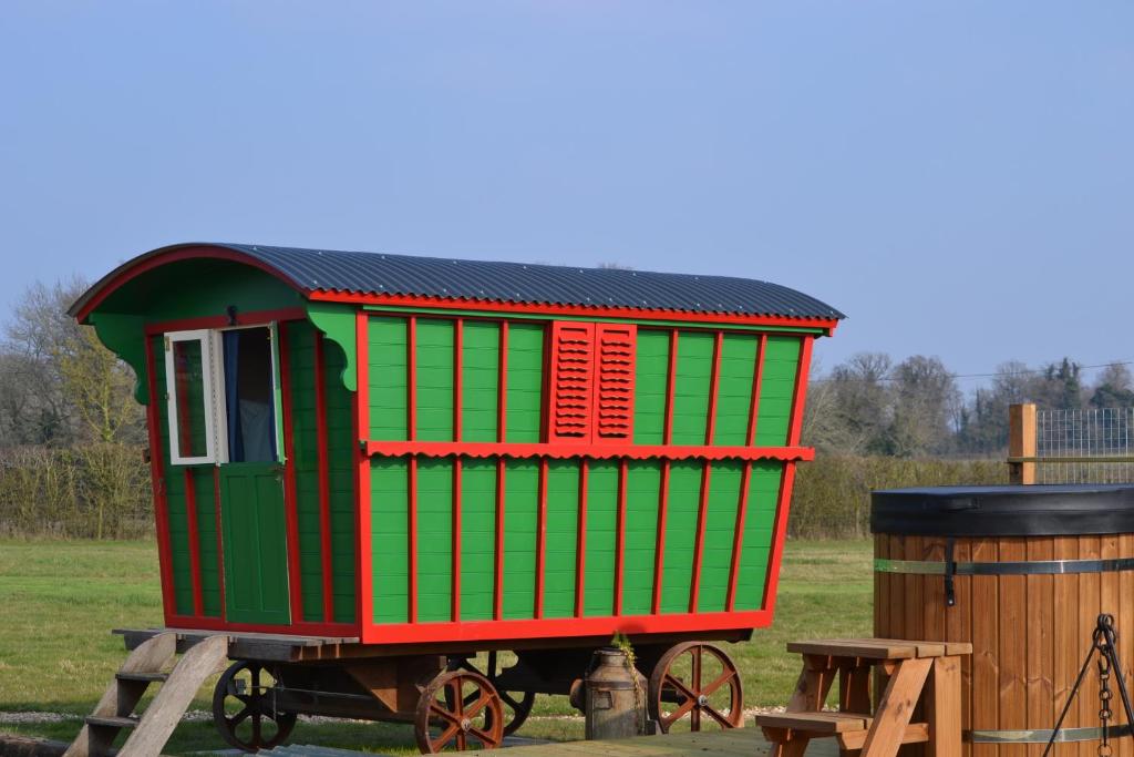 a green and red train car sitting next to a barrel at Isabelle Shepherd's hut in Hethersett