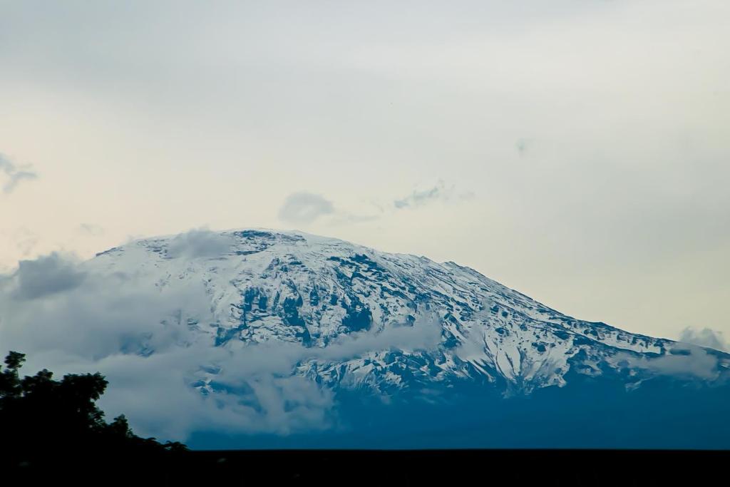 a snow covered mountain with clouds in the background at Kiusa Badget Hotel in Moshi