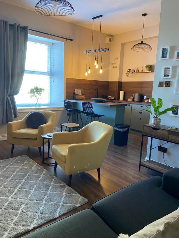 a living room with yellow chairs and a kitchen at Warm Spacious apartment in Pembroke Dock