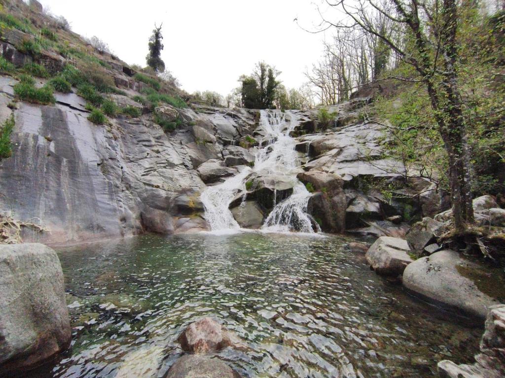 a waterfall on the side of a rocky mountain at La flor del cerezo in Piornal
