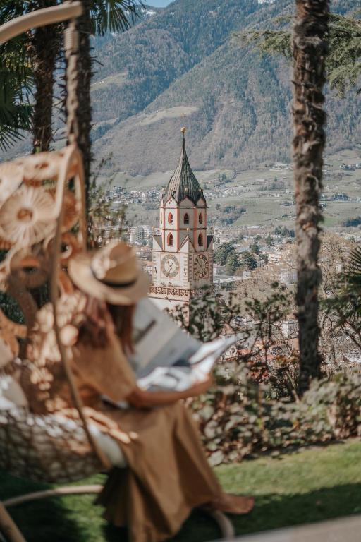 a woman sitting in a chair looking at a building with a clock tower at Villa Hochland in Merano