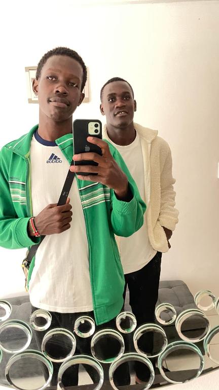 two men standing in front of a mirror holding a cell phone at Karibu comfort in Kisumu