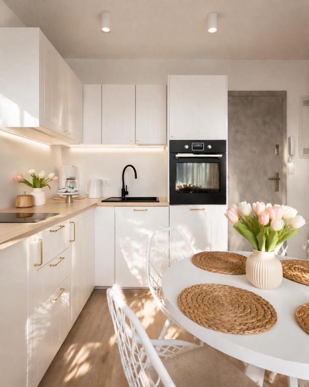 a kitchen with white cabinets and a table with flowers on it at Baltic Harmony - Easy-Rent Apartments in Pobierowo