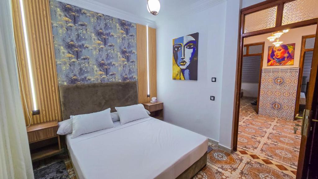 a bedroom with a white bed and a painting on the wall at Central Premium Holiday Homes - Marché, Corniche & Océan à pied in Larache