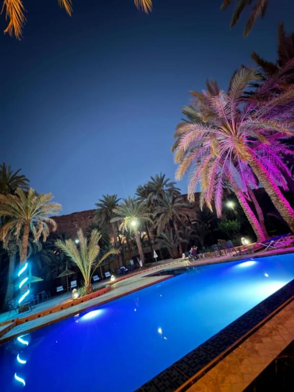 a swimming pool with palm trees at night at GITE LA GROTTE VALLEE in Aoûtouss