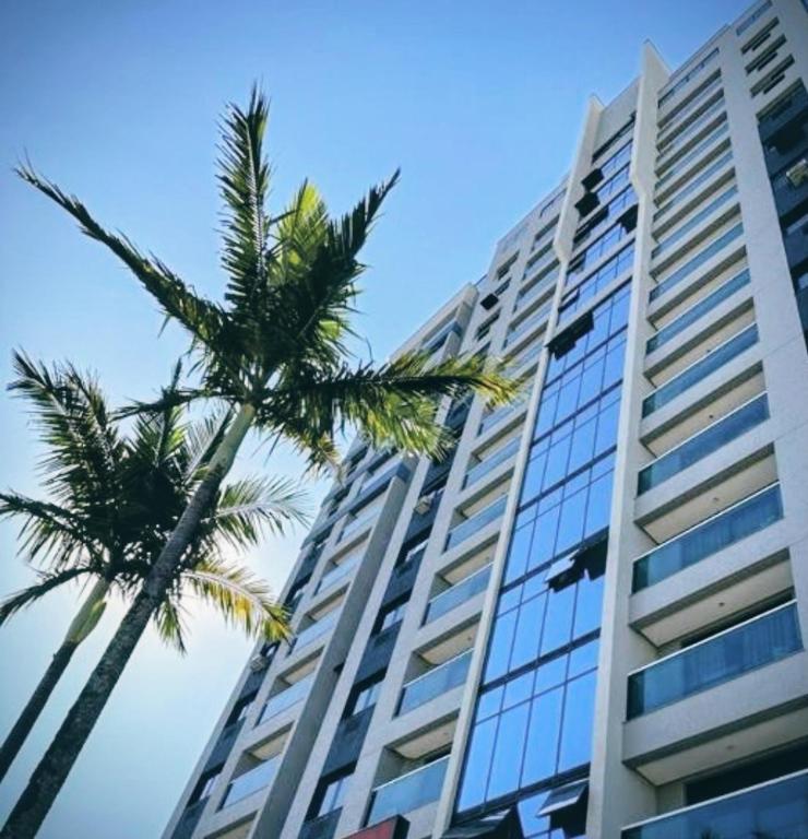 a tall building with palm trees in front of it at Apart Hotel 48 in Mogi das Cruzes