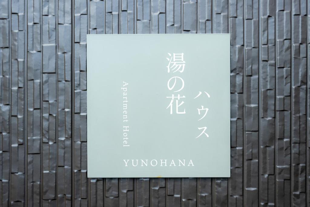a white sign on a wooden wall withwegian writing on it at あわら湯のまち駅から徒歩3分の湯の花ハウス in Awara