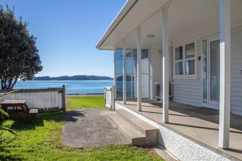 a porch of a house with a bench and the water at Rehutai Beach House in Paihia