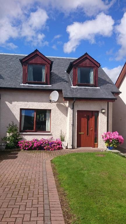 a white house with red doors and pink flowers at Holiday House Kinveachy in Aviemore