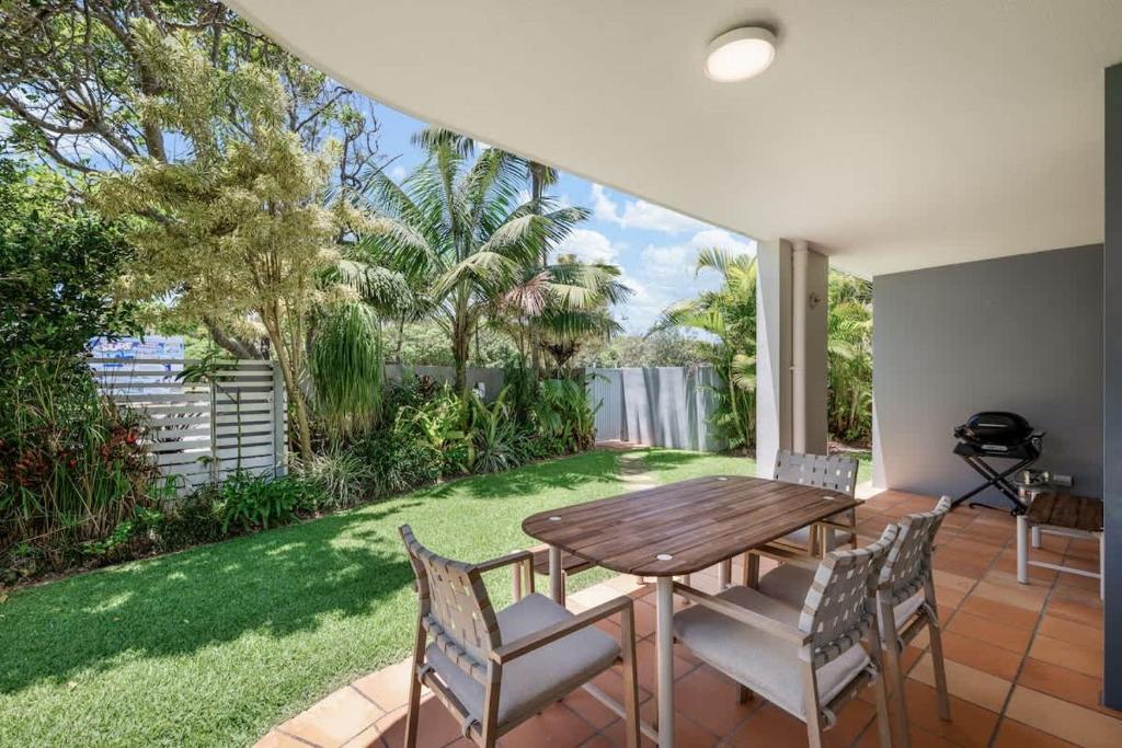 a patio with a wooden table and chairs and a lawn at Pawfect Coastal - Pet friendly Beachfront Pool in Marcoola