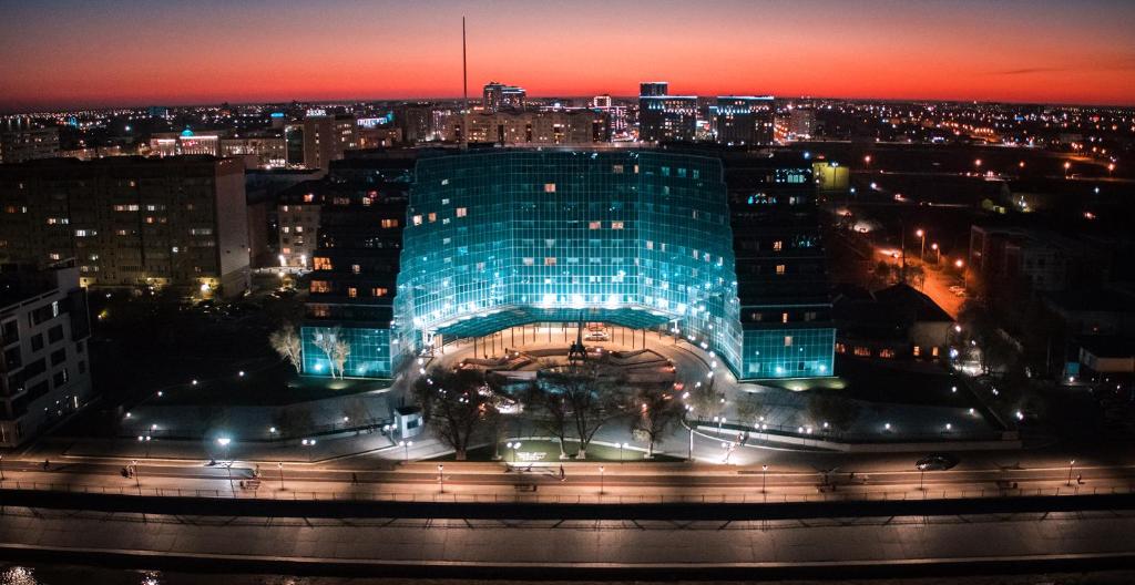 a large glass building with a city at night at River Palace Hotel in Atyrau