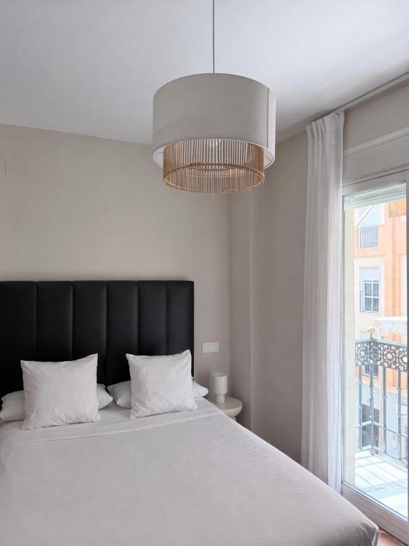 a bedroom with a bed with a black headboard and a window at La Vega Rooms in Huelva