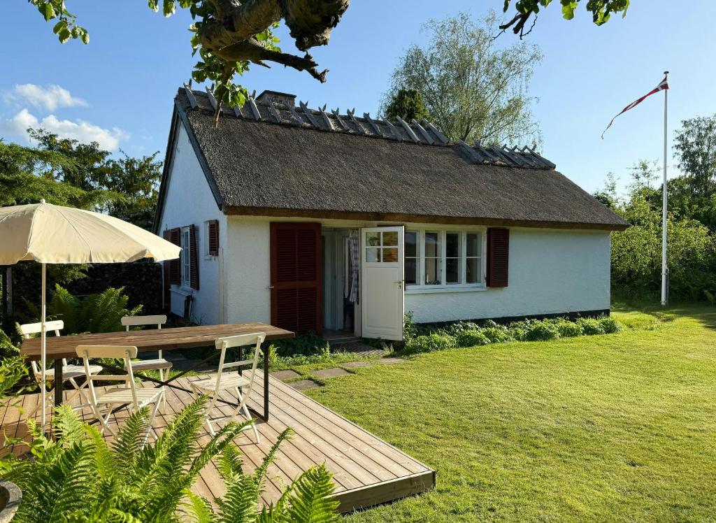 a small white cottage with a table and an umbrella at Thatched Cottage Near Dronningmølle Beach in Dronningmølle