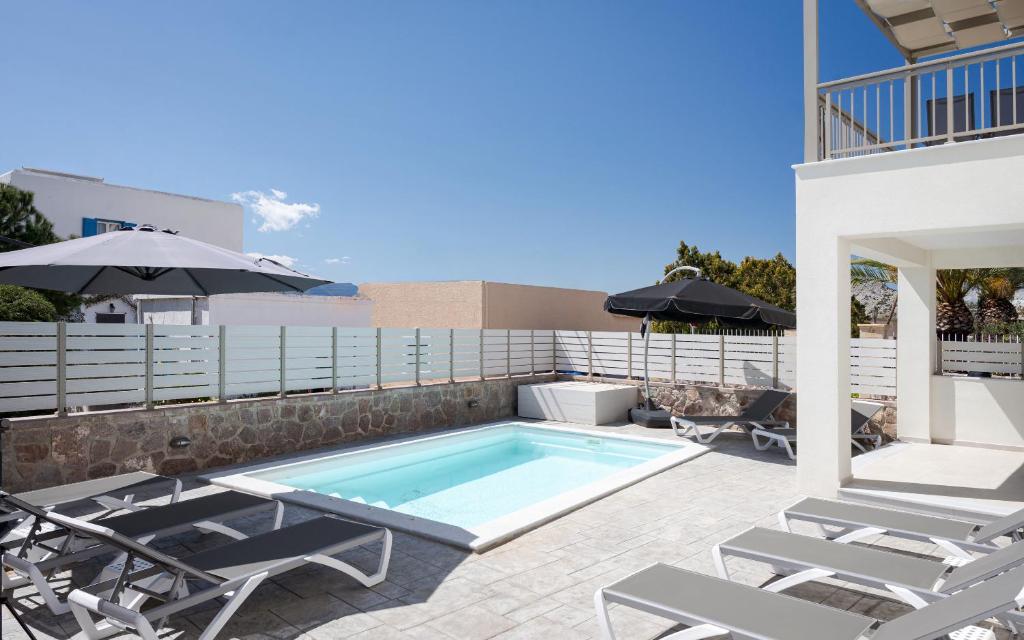 a swimming pool with two chairs and an umbrella at Fasma Suites in Perdika