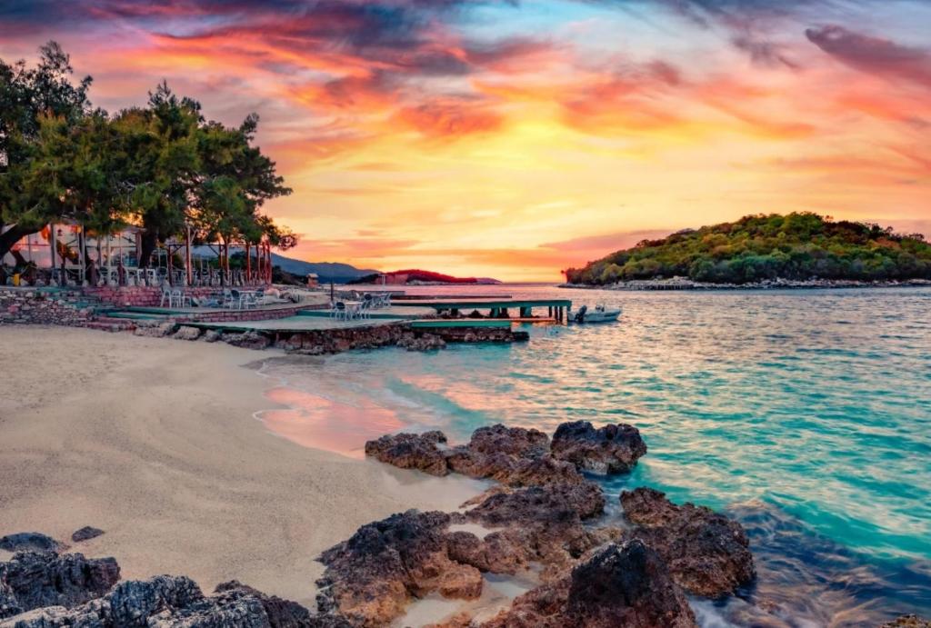 a sunset over a beach with a pier and trees at Guest House Gerard in Ksamil